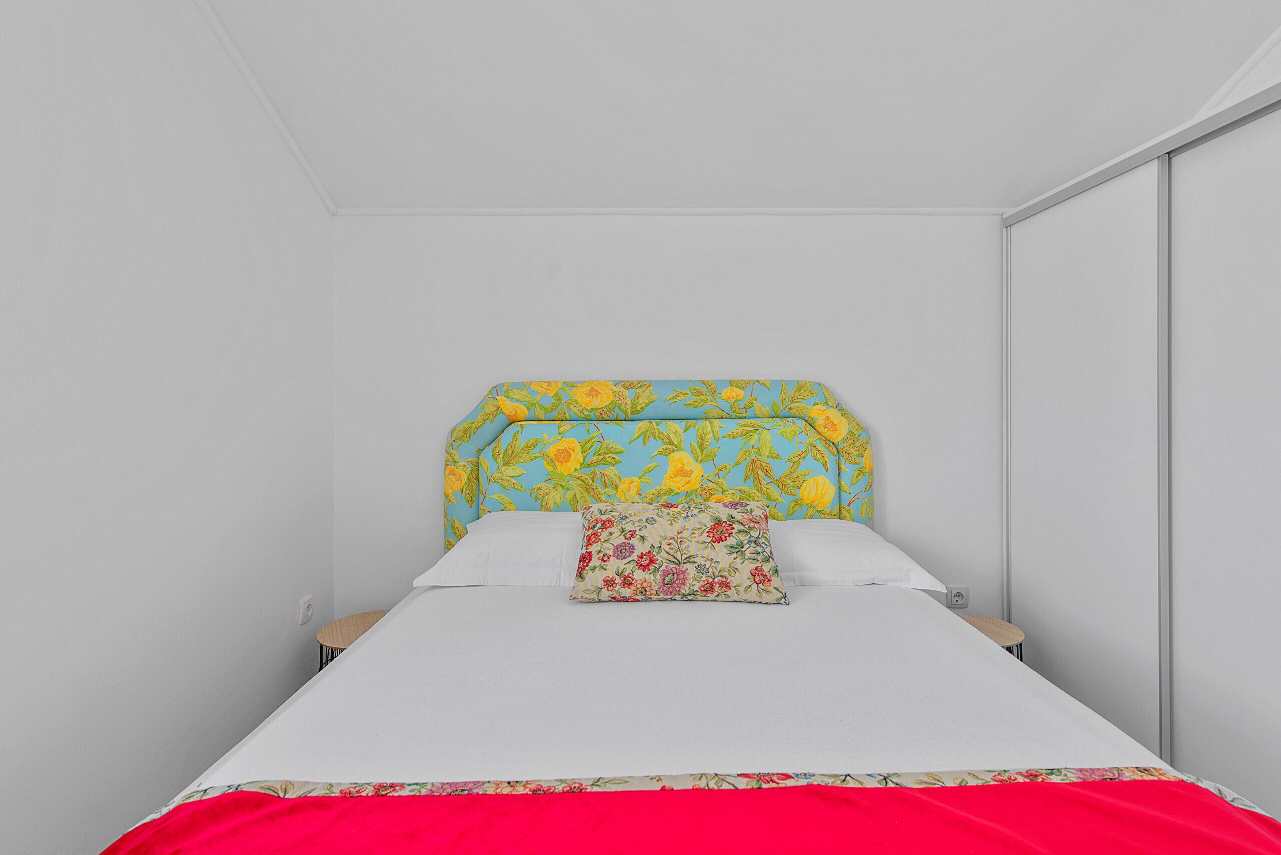 Una cama con cabecera floral, una colcha roja y una almohada con estampado floral.