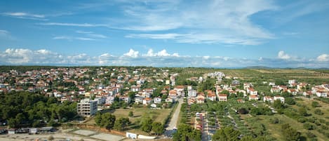 Vista aérea de un pueblo costero con un puerto deportivo, edificios residenciales y colinas verdes al fondo.