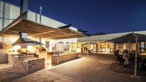 An outdoor patio area with stone flooring, a brick counter, and tables under umbrellas. - Safari Lodge (Windhoek)