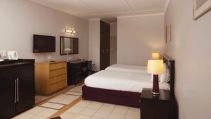 A hotel room with a bed, a desk, a wardrobe, a television, and a bathroom door. - Safari Lodge (Windhoek)