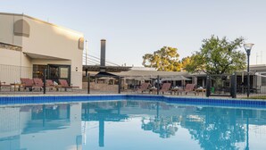 A swimming pool with lounge chairs and a covered seating area. - Safari Lodge (Windhoek)