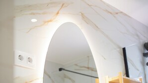 Une salle de bain aux murs recouverts de marbre, avec une étagère en bois et une arche blanche.