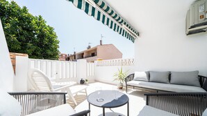 Une terrasse extérieure ensoleillée, dotée de meubles en osier, d’une table ronde et d’un canapé.