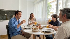 Un grupo de personas sentadas alrededor de una mesa redonda con platos, vasos y una cesta de pan.