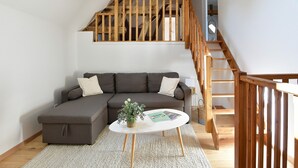 A modern living room with a sectional sofa, a small coffee table, and a wooden staircase. - Cottage 'La Mottelette' with Private Terrace and Garden (Forest-Montiers)