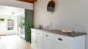 A kitchen with white cabinets, a wooden countertop, a round wall clock, and a door leading to a garden. - Cottage 'La Mottelette' with Private Terrace and Garden (Forest-Montiers)