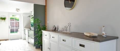 A kitchen with white cabinets, a wooden countertop, a round wall clock, and a door leading to a garden.