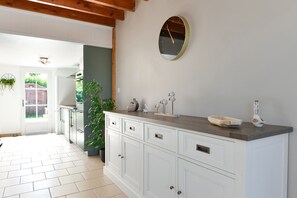 A kitchen with white cabinets, a wooden countertop, a round wall clock, and a door leading to a garden.