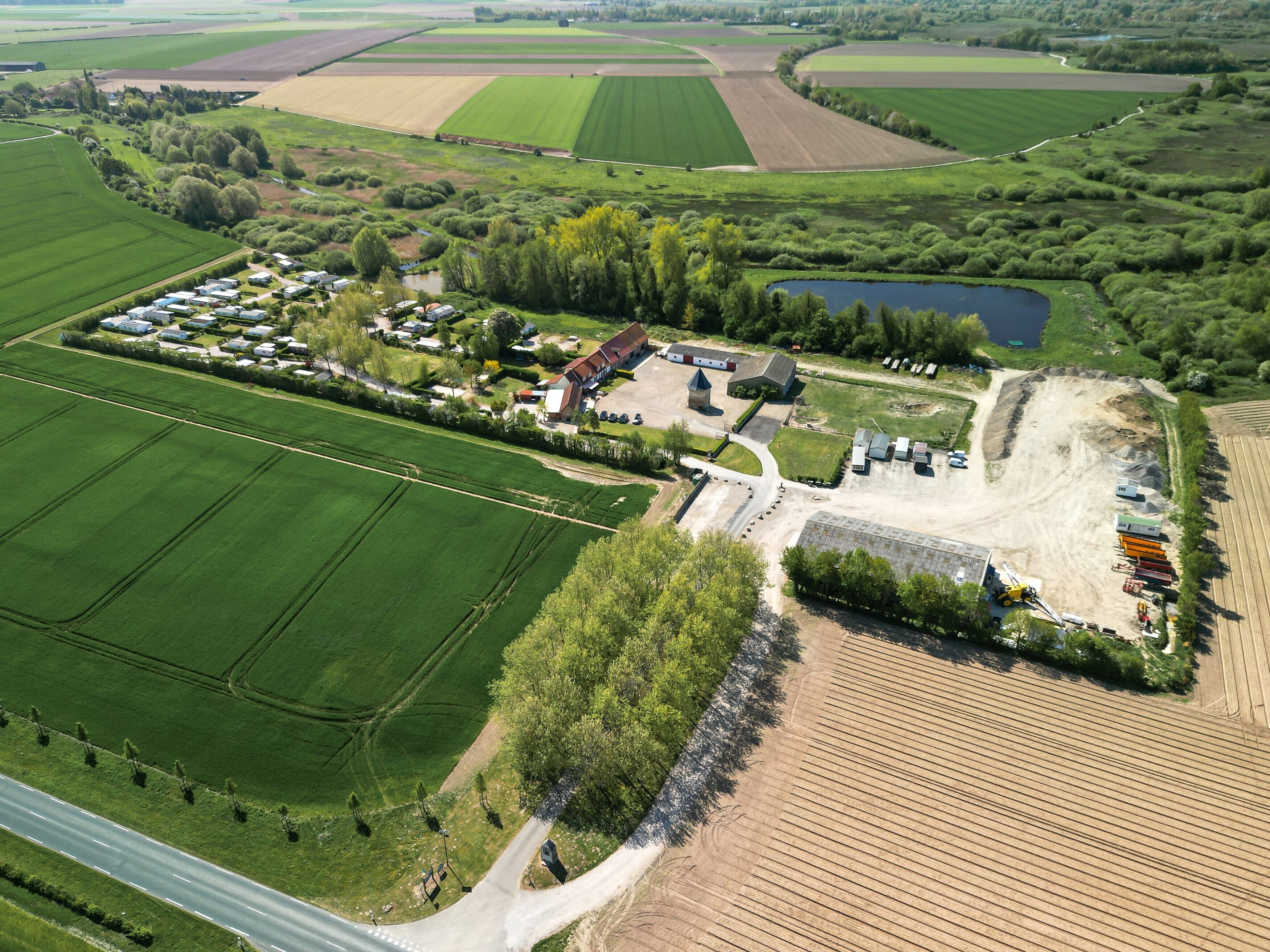 Vue aérienne d’une propriété rurale comprenant des champs, un petit lac et un ensemble de bâtiments avec un parking.