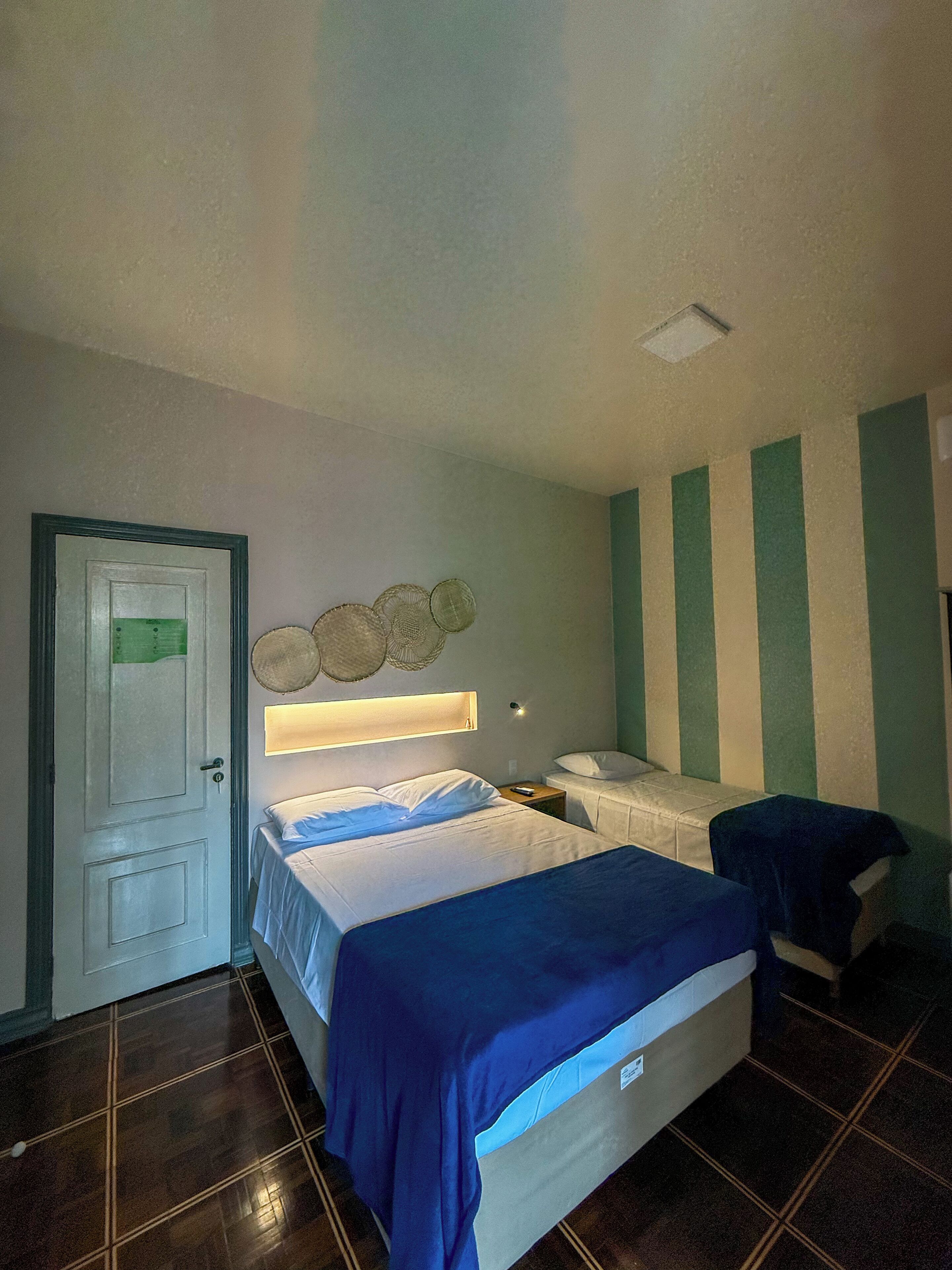 A hotel room with a bed, a bedside table, a nightstand, a lamp, and a door.