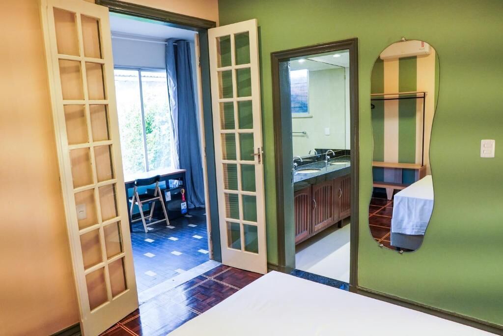 A room with a large bed, a bathroom with a mirror and sink, and a view through an open door.