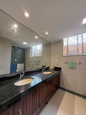 A bathroom with a double sink vanity, a large mirror, and a window with decorative iron bars.