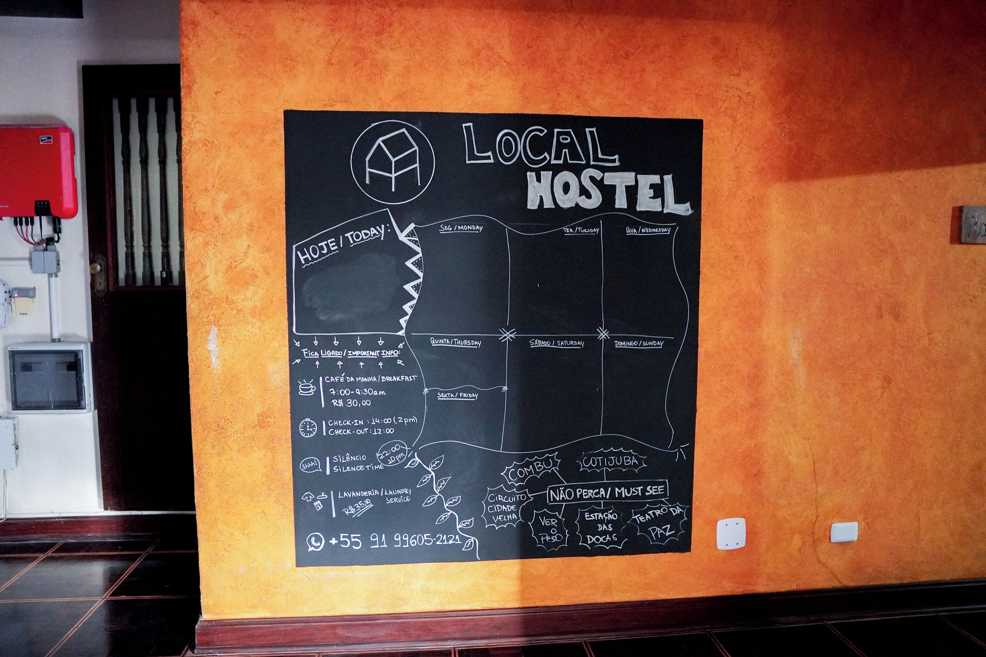 A wall with a chalkboard displaying a hostel's schedule, amenities, and contact information.