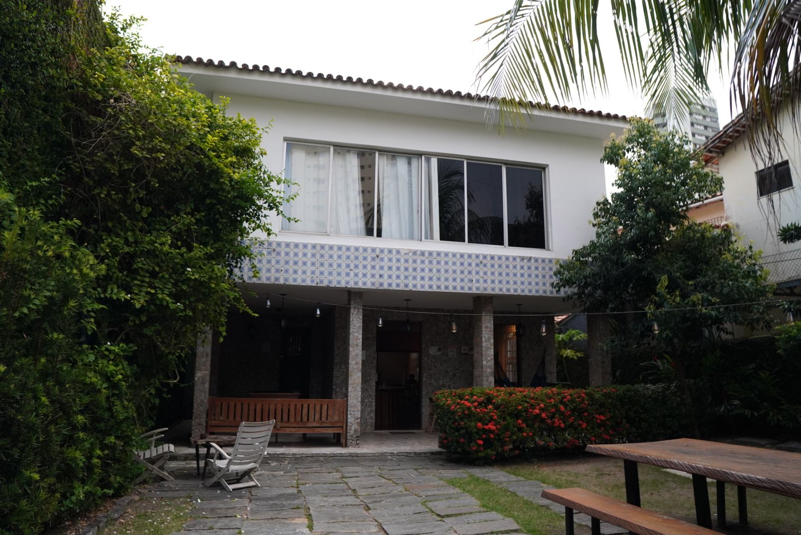 Uma casa de dois andares com varanda coberta, piso de pedra e um banco.