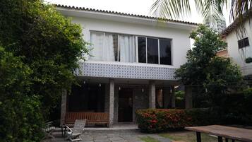 Uma casa de dois andares com varanda coberta, piso de pedra e um banco.