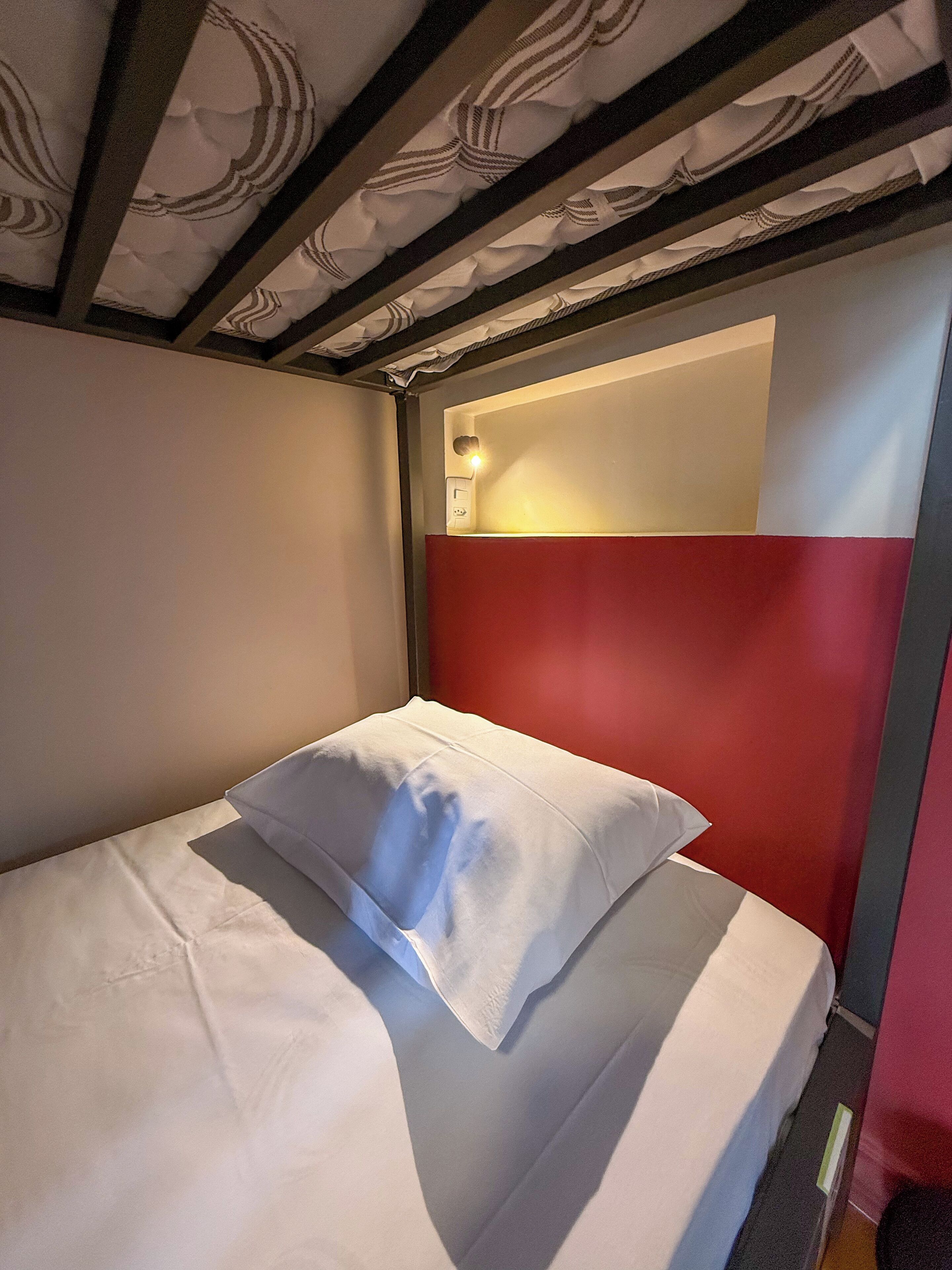 Una cama individual con ropa de cama blanca y una pared de acento roja.