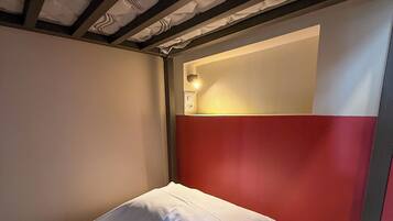 A single bed with white bedding and a red accent wall.