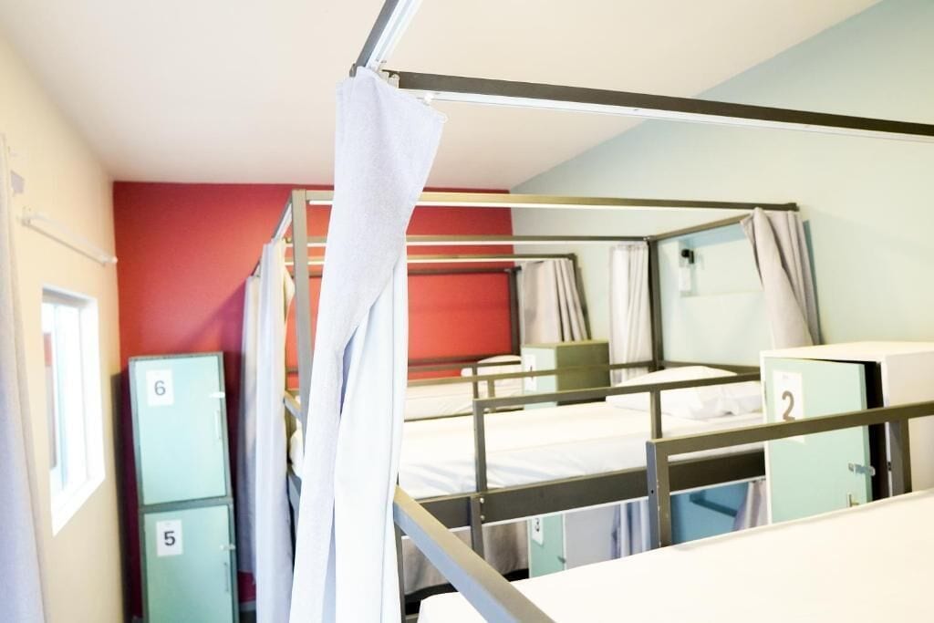 Une chambre de dortoir avec des lits superposés, des casiers numérotés et un rideau.