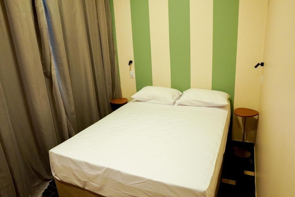 A single bed with white bedding, two bedside tables, and a curtain.