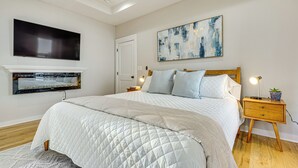 A bedroom with a large bed, a mounted TV, a painting, and a bedside table with a lamp. - Walk to Beltline: Wfh-friendly Hub w/ Yard! (Atlanta)