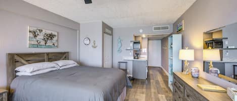 Un dormitorio con cama, ventilador de techo, kitchenette y baño.
