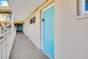 A corridor with a blue door, a balcony with white railings, and a stairway leading to an upper level. - Oceanfront Gem - Walk to Daytona Beach Pier! (Daytona Beach)