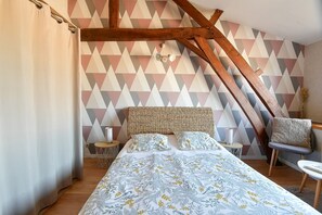 Une chambre à coucher comprenant un lit, une chaise, une petite table et un mur orné d’un motif géométrique.