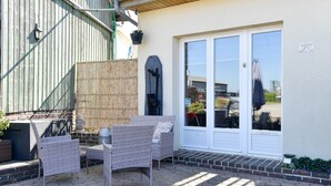 Une terrasse dotée de meubles en osier, d’une clôture en bambou et d’un bâtiment blanc avec une porte-fenêtre coulissante.