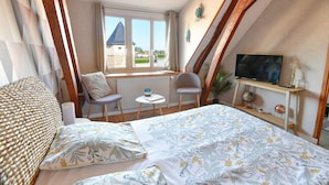 Une chambre à coucher avec un lit, deux chaises, une petite table, un téléviseur et une fenêtre donnant sur un beau paysage.