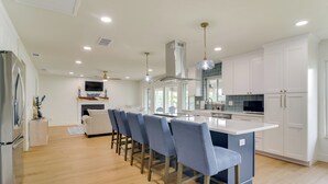 A modern kitchen with a central island, bar stools, and white cabinetry. - Riverfront Basecamp to Boat Fish Chase Sunsets (Ruskin)