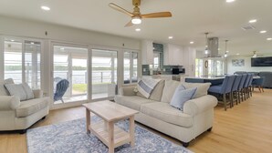 A spacious living room with a large sofa, a coffee table, and a view of a lake through large sliding doors. - Riverfront Basecamp to Boat Fish Chase Sunsets (Ruskin)