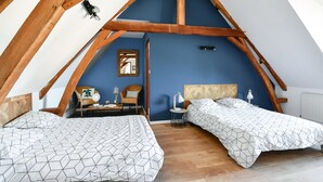 A bedroom with a sloped ceiling, two beds with geometric-patterned bedding, a wooden chair, a small table, and a mirror on the wall.