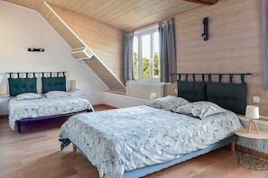 Une chambre avec deux lits, un plafond en pente, une fenêtre avec des rideaux, une lampe de chevet et un radiateur.