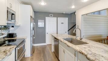 A modern kitchen with white cabinets, a granite countertop, stainless steel appliances, and a wooden floor.