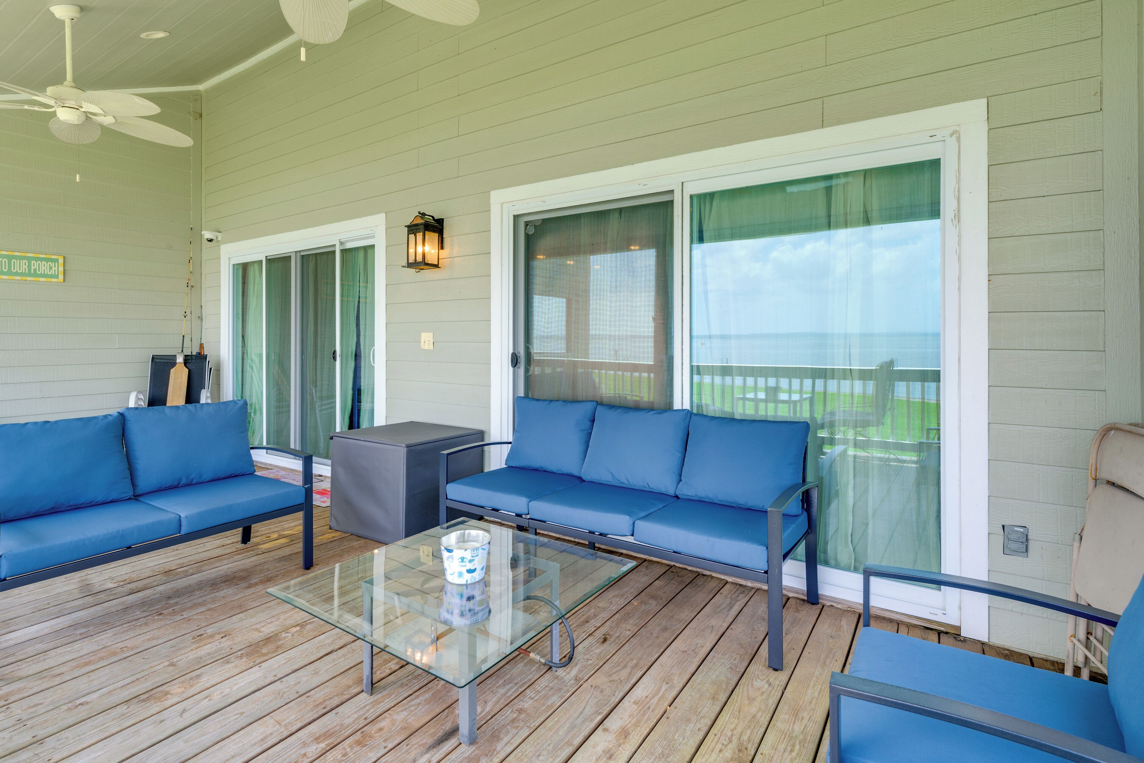 A covered porch with a glass coffee table, blue sofas, and a ceiling fan.