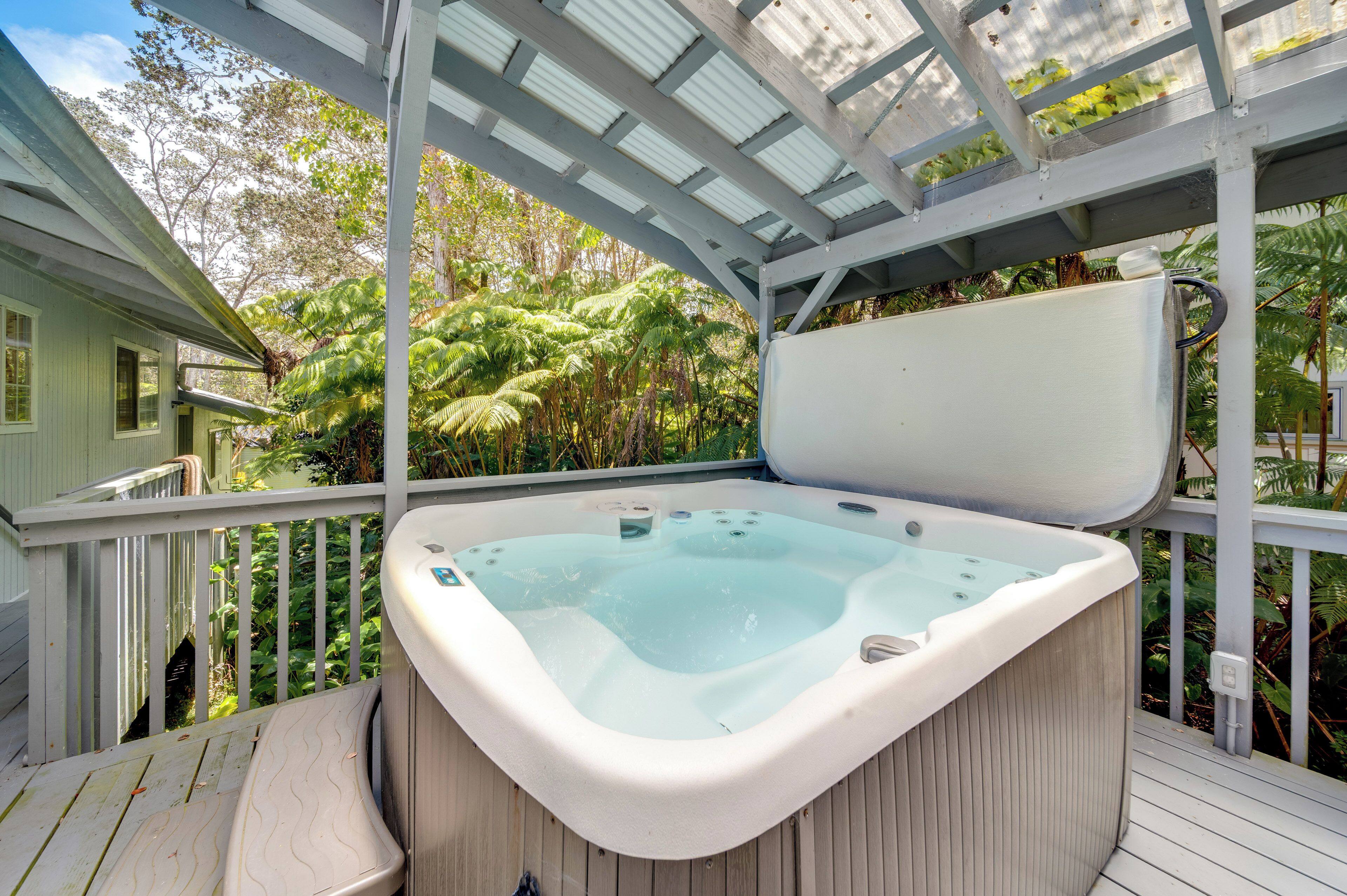 A hot tub on a wooden deck with a glass ceiling, surrounded by lush greenery.