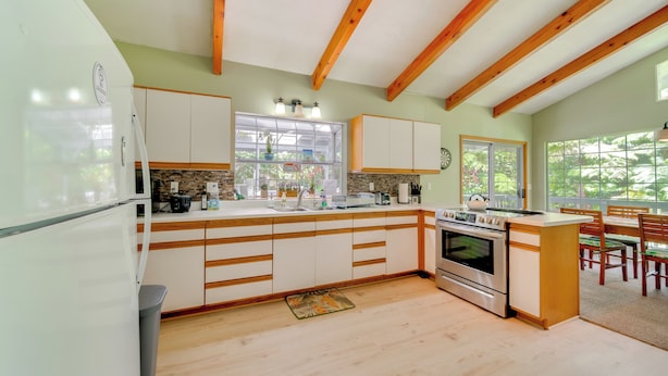 A kitchen with wooden beams, white cabinets, a large island, and a dining area with a view. - Private Hot Tub & Deck: Tranquil Volcano Hideaway! (Volcano)