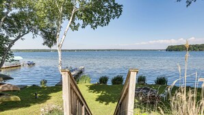 Une terrasse en bois qui mène à un lac où sont amarrés des bateaux, le tout entouré de verdure et sous un ciel dégagé.
