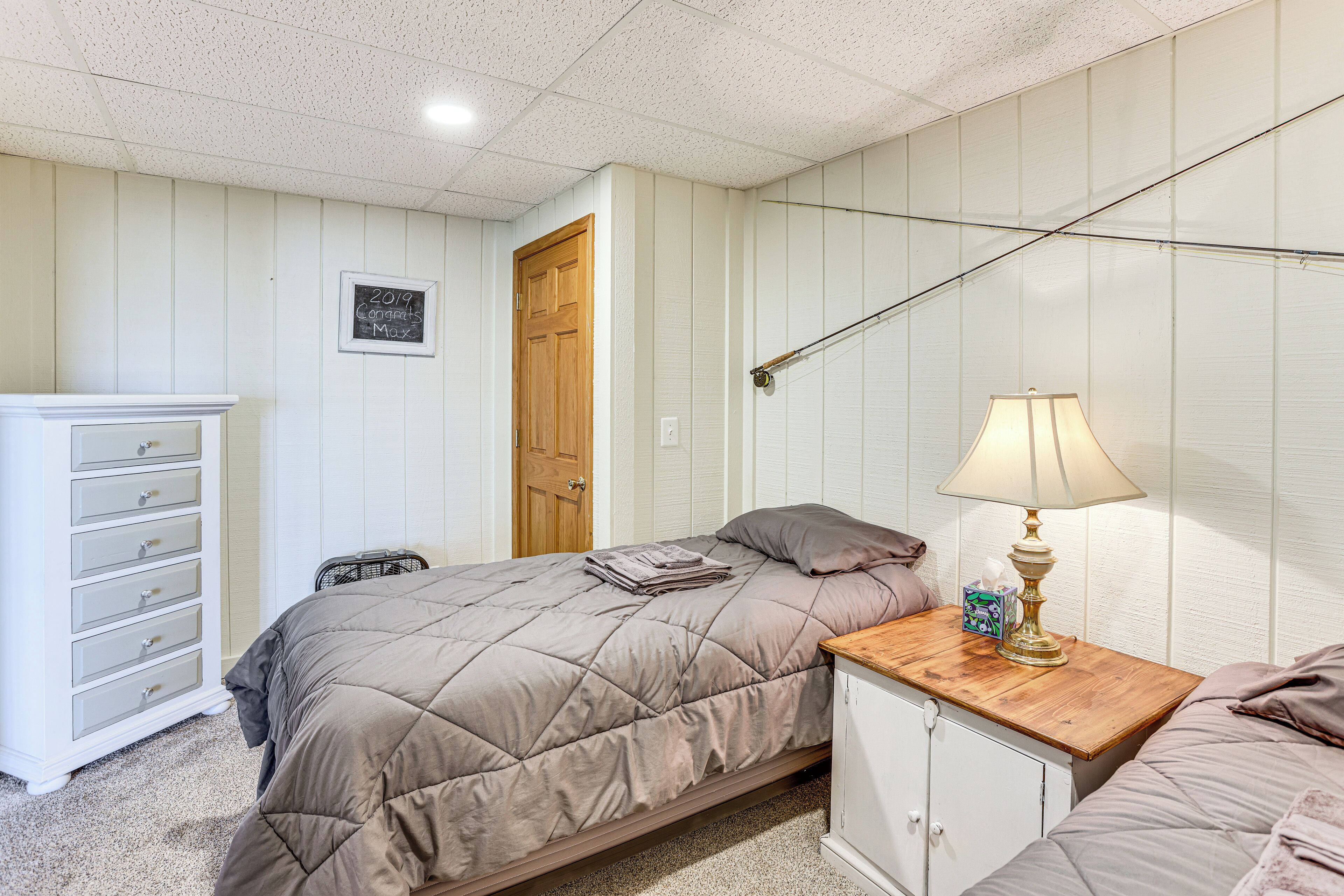 A bedroom with a bed, a nightstand with a lamp, a dresser, and a door.