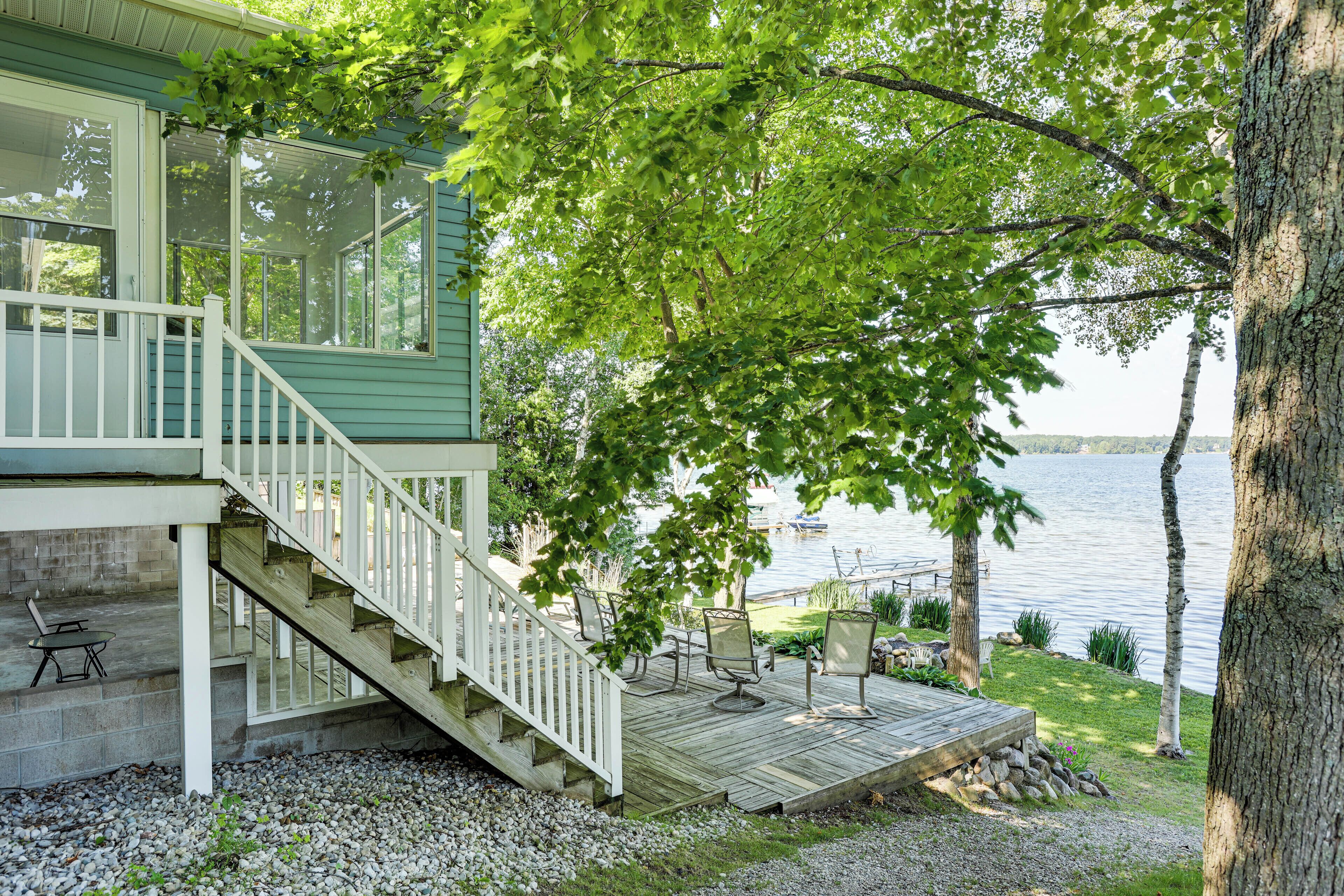A lakeside cabin with a wooden deck, outdoor seating, and a staircase leading to a covered porch.