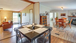 Uma sala de jantar ampla com uma grande mesa de madeira e cadeiras combinando, uma área de estar aconchegante com um sofá e poltrona, e uma lareira ao fundo.