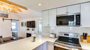 Una cocina moderna con armarios blancos, microondas integrado, estufa de acero inoxidable y una mesa de comedor de madera.