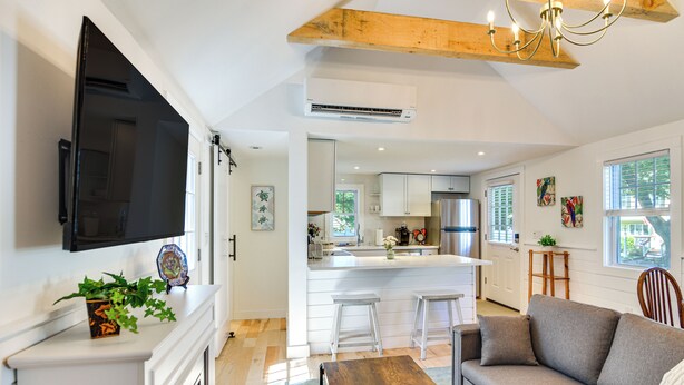 Una cocina moderna con armarios blancos, una isla central y un comedor con mesa de madera y taburetes de bar.
