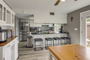 A modern kitchen with white cabinets, a stainless steel refrigerator, a microwave, and a coffee machine. There are four bar stools and a wooden table. - Townhome 10 Mi to Wpafb & Dayton! (Dayton)