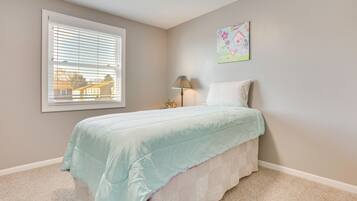 A bedroom with a bed, a window with blinds, a lamp, and a wall art piece.