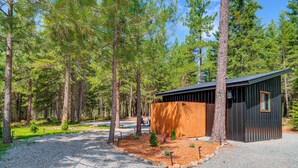 Una cabaña moderna con fachada de madera y techo metálico, rodeada por un bosque de altos pinos.