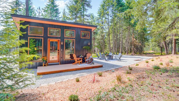 Une cabane moderne dotée de grandes fenêtres, d’une terrasse et d’un espace salon extérieur.