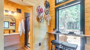 Interior de una cabaña de madera con baño, zona de comedor y un perchero.