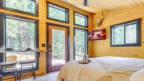 Une chambre confortable dans un chalet, avec un grand lit, un téléviseur fixé au mur et un coin repas comprenant une table et des chaises.