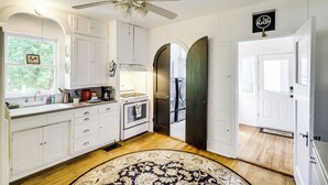A kitchen with white cabinets, a stove, and a ceiling fan. There is a rug on the floor and a door with a doormat.